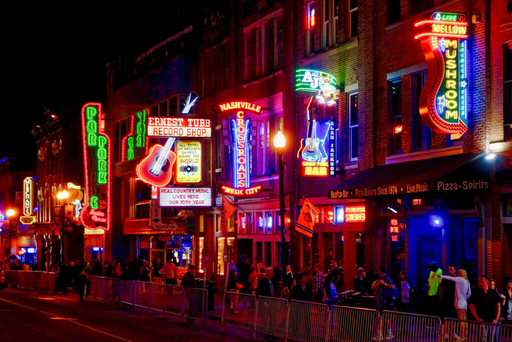 Street in Nashville, Tennessee at night lit up with neon signs advertising music clubs
