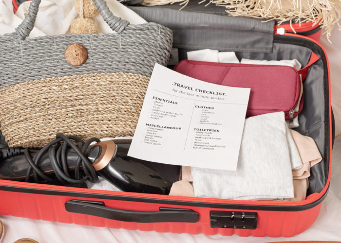 Overhead view of packed suitcase full of summer travel items and travel checklist